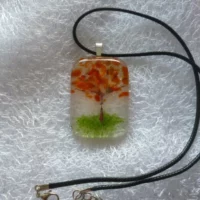 Autumn tree pendant, clear glass copper colour tree trunk and shades of orange for the leaves / petals, green colour for the grass. Hangs from a black cord necklace.