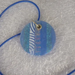 Large round blue dichroic glass pendant. Stripes of dichroic glass showing the sparkle in the blue, flashes of gold, pink with blue & white pattern glass. Sterling silver grommet and jump ring and hangs from a blue cord necklace.