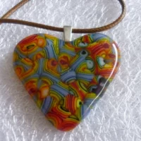 Close up of heart pendant with colours of blue, red, green, black, yellow. All different shapes within the pendant, lines, stripes, arcs looking a bit like layers. 925 sterling silver bail and brown cord necklace.