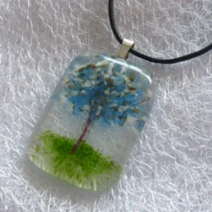 Clear glass pendant with blue and white for the leaves and petals, copper colour for the trunk and green for the grass.