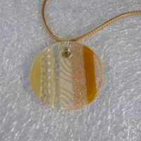 Close up of dichroic glass round pendant. Stripes of sparkly dichroic glass with flashes of gold and silver, along with stripes of tan coloured glass, beige & white screen printed glass. 925 sterling silver grommet with jump ring and hangs from a gold coloured cord necklace.