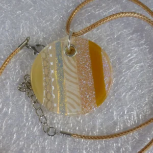 Round dichroic glass pendant with gold coloured cord necklace. Pendant shows stripes of dichroic with flashes of gold and silver. 925 grommet and jump ring attached.