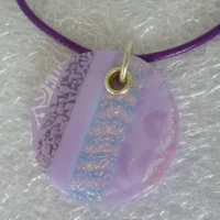 Close up of round lilac dichroic glass pendant at an angle.