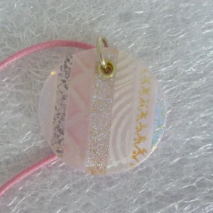 Large round pink dichroic glass pendant. Stripes of dichroic giving flashes of silver and gold, 925 sterling silver grommet and jump ring and hangs from a pink cord necklace.
