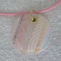Unique pink round dichroic glass pendant close up. Stripes of pink glass, dichroic glass, and screen printed pink and white glass. 925 sterling silver grommet and jump ring, hangs from a pink cord necklace.