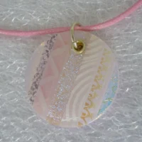 Unique pink round dichroic glass pendant close up. Stripes of pink glass, dichroic glass, and screen printed pink and white glass. 925 sterling silver grommet and jump ring, hangs from a pink cord necklace.