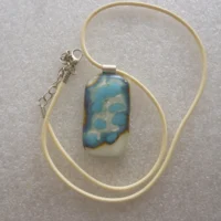 Cream pendant with turquoise and silver pattern on top, 925 sterling silver bail and hangs from a cream cord necklace.