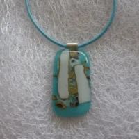 Turquoise blue reactive glass pendant with white and brown pattern made by the chemical reactions within the glass and hangs from a blue cord necklace.