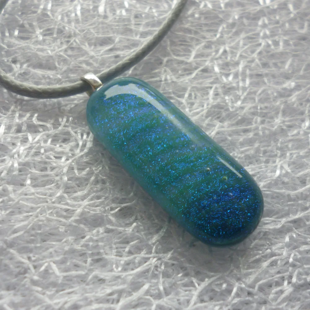 Sparkly blue dichroic glass pendant, with the bottom of the pendant darker in colour than the top. 925 sterling silver bail and grey cord necklace.