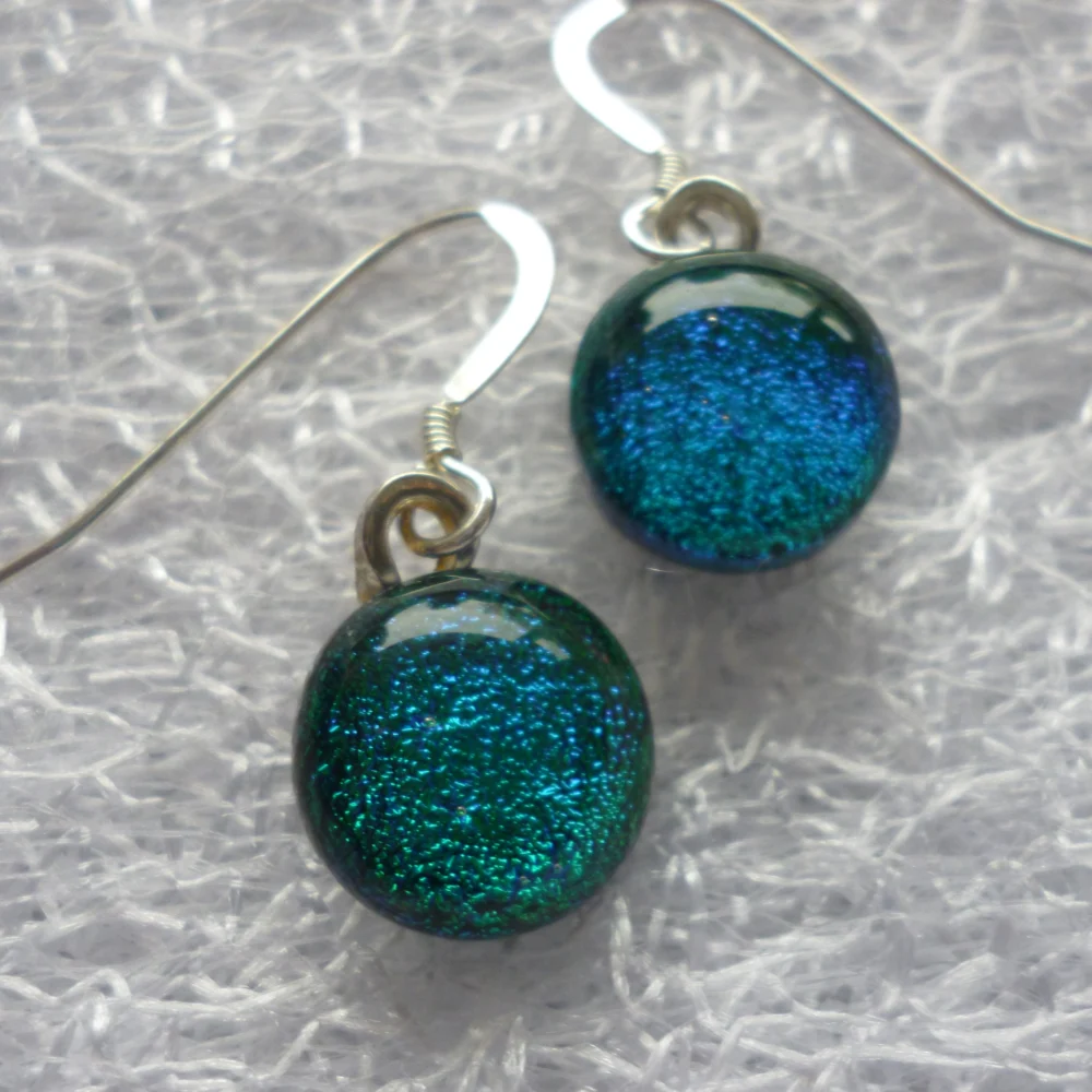 Close up of round green dichroic glass cabochons that are very sparkly with 925 silver ear wires. Depending on the light these cabochons can look green or blue.