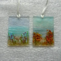 Two seaside suncatchers with flowers made of fused glass, glass powder, frit and stringers. Hole at the top with a white ribbon threaded through.