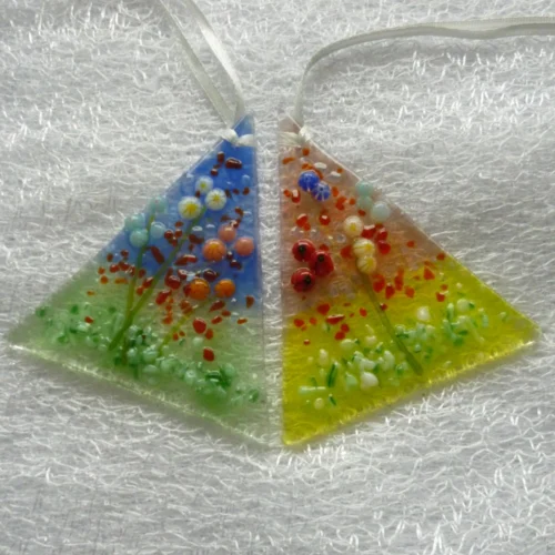 Two small flower suncatchers with flowers in red, blue, pink, orange, white. Fused glass suncatcher is triangular in shape with background colours in pink and green, blue and green.