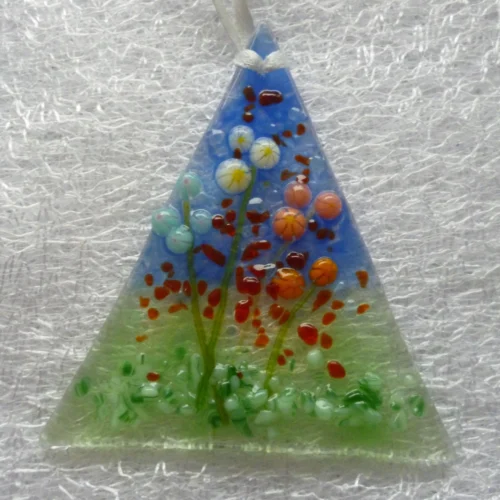 Small flower suncatcher with a background of blue and green, and white, blue, pink and orange flowers. Hanging from a white ribbon.