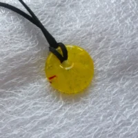 Round yellow donut pendant necklace with a speck of red. Black cord necklace threaded through.