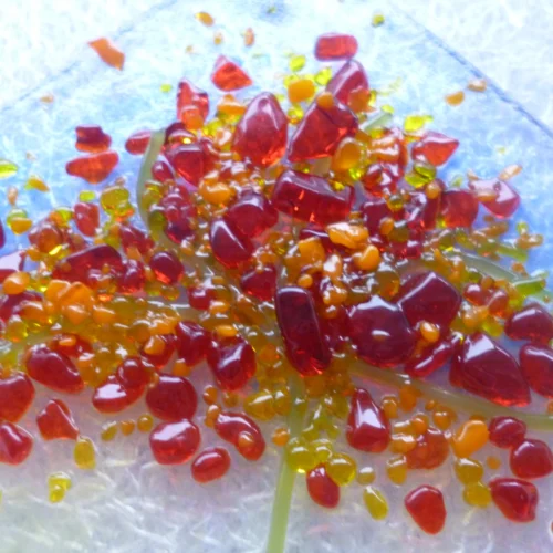 Close up of small suncatcher with autumn colours of red, orange, yellow and green in the design of a tree. This fused glass suncatcher is very tactile.