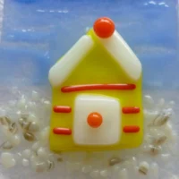 Close up of yellow beach hut small fused glass suncatcher. A very tactile design with red stripes, white door and roof trimming.