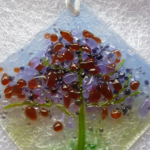 Close up of small suncatcher with spring inspired colours of plum, lilac, purple and green in the design of a tree. This fused glass suncatcher is very tactile.