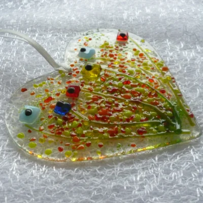 Side view of floral heart shaped suncatcher with the light shining on it. This is a very tactile suncatcher in colours of blue, red, green, orange and yellow.