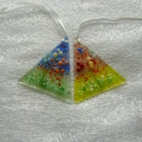 Two small flower suncatchers with flowers in red, blue, pink, orange, white. Fused glass suncatcher is triangular in shape with background colours in pink and green, blue and green. Hangs from a white ribbon.