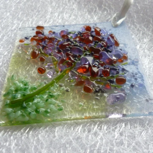 Side view of spring tree designed small suncatcher. This is a very tactile design with colours of lilac, purple, plum and green. Hole at the top of the suncatcher with a white ribbon threaded through to hang from.