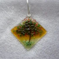 Diamond shaped fused glass suncatcher hanging from a white ribbon. With red and green glass used for leaves and blossoms of the tree. Hanging from a white ribbon.
