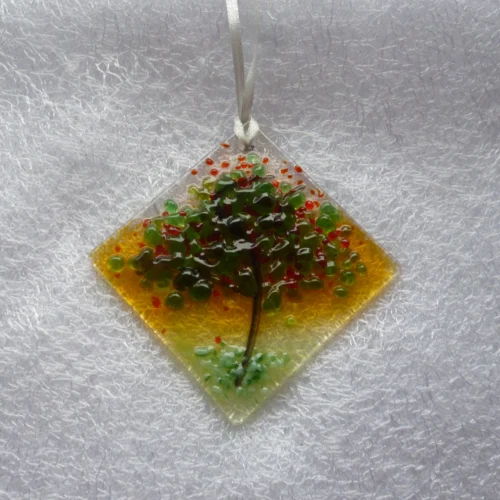 Diamond shaped fused glass suncatcher hanging from a white ribbon. With red and green glass used for leaves and blossoms of the tree. Hanging from a white ribbon.