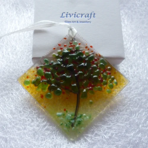 Diamond shaped fused glass suncatcher with white ribbon leaning against a gift box.