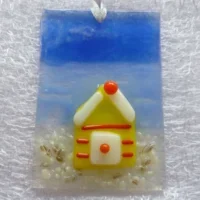 Rectangle shaped small fused glass suncatcher with yellow beach hut, blue and white background and hangs from a white ribbon.
