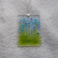 Rectangle glass suncatcher with blue and turquoise beads to create flowers. Hanging from a white ribbon.