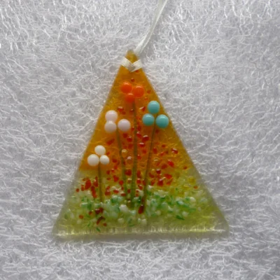 triangular fused glass suncatcher with flowers on a background of orange and green. Flowers are glass beads in colours of orange, turquoise, pink and white. Hangs from a white ribbon.