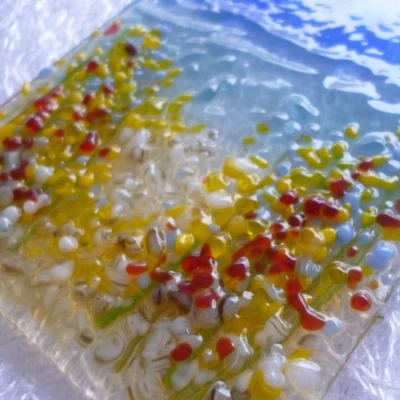 Close up of small coastal suncatcher with red, orange, blue and white tactile flowers.