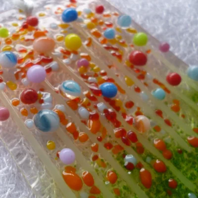 Close up of very colourful glass suncatcher with beads in yellow, blue, pink, red, green and long stems. Frit in red and orange for decoration.