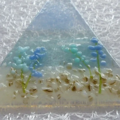 Close up of coastal suncatcher with blue and turquoise flowers on a background of blue. This is a very tactile design.
