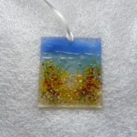 Small square fused glass coastal suncatcher with background of blue and turquoise, with tactile flowers in red, blue, orange and white flowers on the beach.