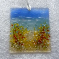 Square fused glass coastal suncatcher with red, blue, orange and white flowers with green stems. Background of blue and turquoise and hangs from a white ribbon.
