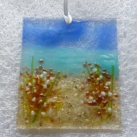 Square coastal suncatcher made in fused glass with plum and white flowers. Hanging from a white ribbon.