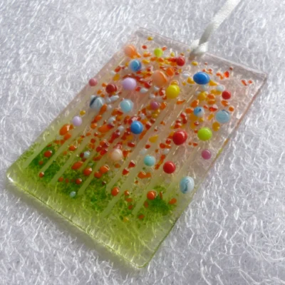 Side view of fused glass suncatcher hanging from a white ribbon.