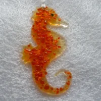 Fused glass seahorse in orange, hanging from a white ribbon.