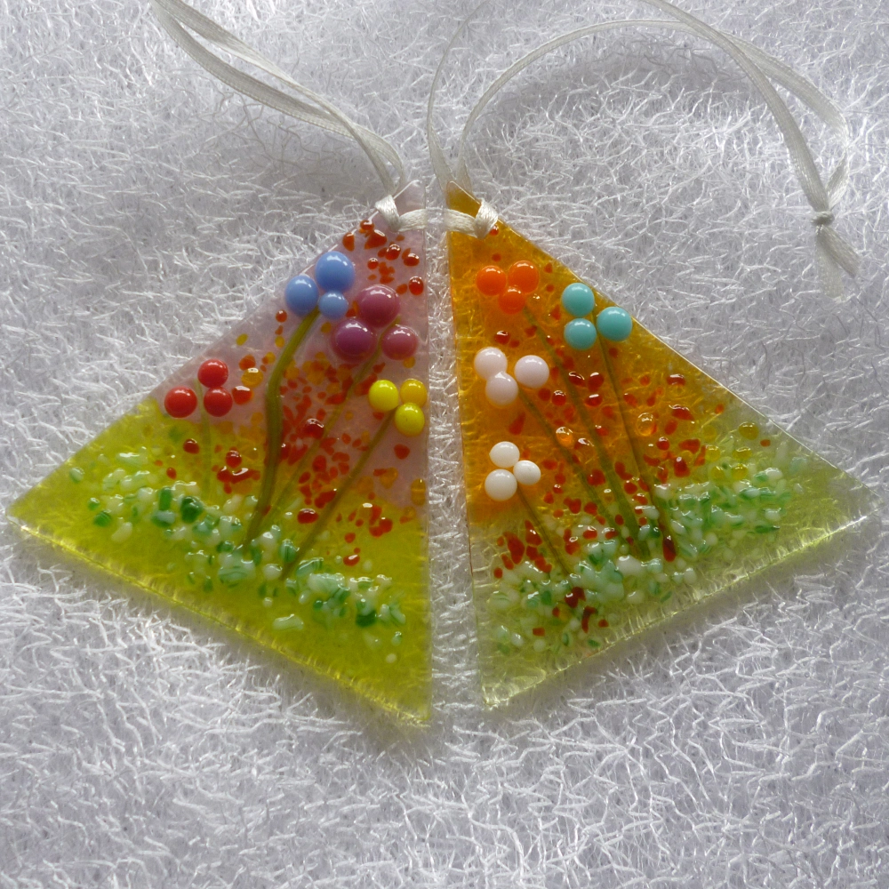 Two small pretty fused glass suncatcher with flowers on top. This is a very tactile design in colours of blue, plum, red, yellow, orange, turquoise, pink and white. Hangs from a white ribbon.