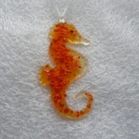 Seahorse made of fused glass with tactile orange frit with white ribbon attached.