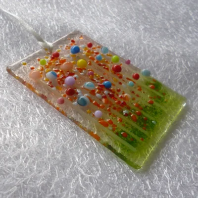 Side view of fused glass suncatcher with very tactile beads for flowers and stringers for stems. Hangs from a white ribbon.