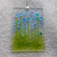 Rectangle shaped glass suncatcher with blue and turquoise beads as flowers with green stringers. Hanging from a white ribbon.