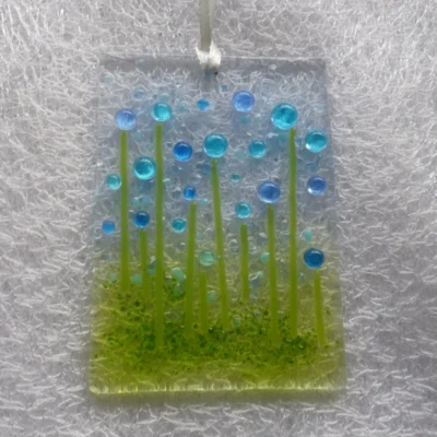 Rectangle shaped glass suncatcher with blue and turquoise beads as flowers with green stringers. Hanging from a white ribbon.