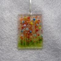 Rectangle fused glass suncatcher hanging from a white ribbon. Multicolour beads have been used to create quirky flowers with stringers for the stems.