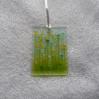 Rectangle fused glass suncatcher with transparent beads for flowers. Frit used for background and decoration and hangs from a white ribbon.
