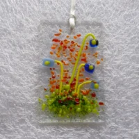 Rectangle shaped fused glass flower suncatcher with blue quirky flowers with green stems. Red, orange and green frit for decoration, hanging from white ribbon.