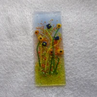 Fused glass flower suncatcher with a background in blue, pink and green. Dark blue and orange quirky square glass flowers with long stems in green and yellow. Frit in orange and green added for decoration. Hangs from a clear cord.