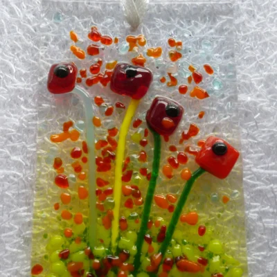 Close up of tactile red flower suncatcher with green stems and red and orange frit for decoration.