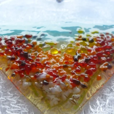 Close up of tactile frit fused on to glass heart suncatcher in colours of red, amber and orange.
