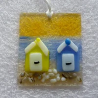 Oblong coastal suncatcher with tactile yellow and blue beach huts trimmed in white. Hangs from a white ribbon.
